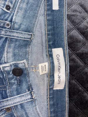 Blå jeans från Calvin Klein Jeans - Snygga ljusblå jeans från Calvin Klein Jeans med klassisk femficksdesign och svarta detaljer på knapparna. Jeansen har raka ben och normal passform, med broderade bakfickor och tydlig logotyp både på läderpatch och etikett. Perfekt för dig som gillar stilrena och tidlösa jeans.