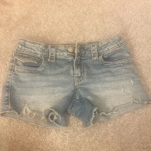 Blå jeansshorts från Gina Tricot - Säljer ett par blå jeansshorts från Gina Tricot som inte säljs längre. Dom är i storlek 152. De har fransiga kanter, slitna detaljer och klassiska fickor både fram och bak. 
