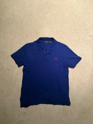 Blå Polo Ralph Lauren piké  - Snygg mörkblå piké från Polo Ralph Lauren i klassisk pikéstil med korta ärmar och krage. Röd broderad logga på bröstet och två knappar vid halsen. (Tröjan är i barnstorlek) passar lite mindre tonåringar! Hör av er vid intresse! (Pris går att diskuteras)🤝
