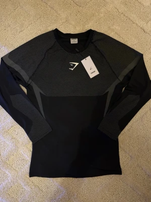 Gymshark Onyx V5 Långärmad Träningströja – Vit & Svart - Gymshark Onyx V5 Långärmad Träningströja – Vit & Svart 👕 Storlek: M 🎨 Färg: Vit med svarta detaljer 👕 Modell: Onyx V5 – långärmad träningströja ✨ Skick: 10/10 – helt ny, aldrig använd 🏷️ Detalj: Originaltag kvar 💎 Märke: Gymshark