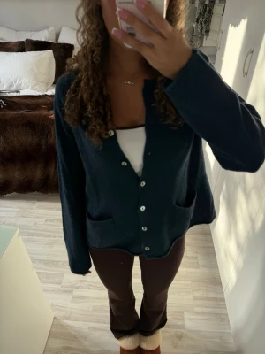 Mörkblå stickad kofta med knappar - Mysig mörkblå stickad kofta med v-ringning och knappar framtill. Koftan har två fickor och långärmade ärmar. Sitter som en s/m 