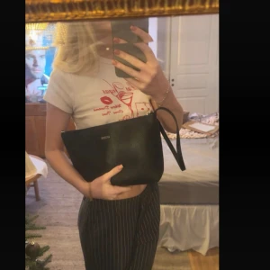 Svart handväska från Guess - Säljer en stilren svart handväska från Guess med enkel design och diskret logga framtill. Väskan är tillverkad i ett slätt skinnliknande material. Perfekt storlek för det viktigaste du behöver ha med dig. Inget kvitto eller så men har inte använt den🩷