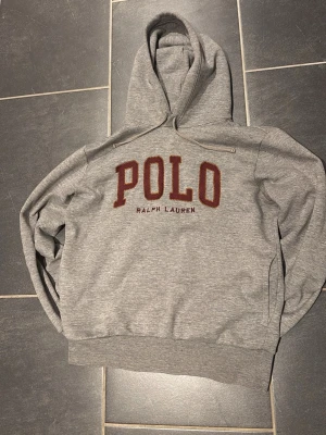Ralph Lauren hoodie - Säljer en fet Ralph Lauren hoodie med den klassiska designen på bröstet. Tröjan är i storlek S för män, den är grå med vinröd text