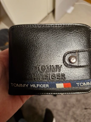 Svart plånbok Tommy Hilfiger - Tommy Hilfiger plånbok i bra skick men jag säljer den eftersom jag tröttnat på den.