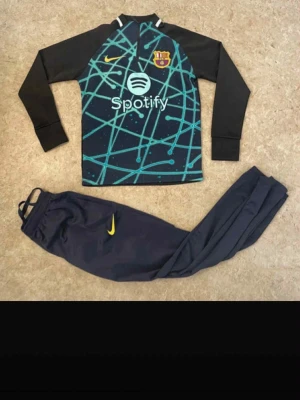 Ingen skor på bilderna - Bilderna visar ett Barcelona träningsset från Nike med långärmad tröja och byxor, men inga skor finns med.