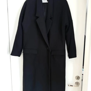 Svart ullkappa från Mango - Svart lång kappa från Mango Suit collection med klassisk krage och enkel knappstängning framtill. Kappan har raka, långärmade ärmar och två fickor med lock. Ullblandning med 70% ull, superfint skick och lyxig! Är tyvärr lite för liten för mig.