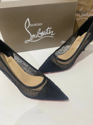 Christian Louboutin svarta pumps, strl 39 - Snygga svarta pumps från Christian Louboutin med ikonisk röd sula. Skorna har spetsig tå, låg klack och är tillverkade i mesh med prickigt mönster och glittriga detaljer. Lyxig känsla med transparenta partier och svarta kanter. Perfekta för dig som vill sticka ut. 8cm klackhöjd
