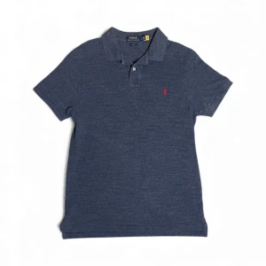 Blå pikétröja Polo Ralph Lauren - Snygg marinblå pikétröja från Polo Ralph Lauren i slim fit-modell. Tröjan har korta ärmar, klassisk krage och två knappar framtill. Det ikoniska röda Polo-logot broderat på bröstet ger en clean och stilren look. Perfekt för dig som gillar enkel och tidlös stil.