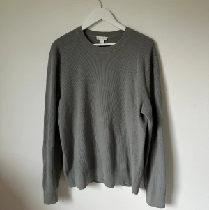 Grå stickad tröja från COS - Snygg grå stickad tröja från COS i storlek M. Tröjan har rund hals, långärmad design och är tillverkad i 100% bomull. Perfekt för dig som gillar enkel och stilren look med lite struktur i materialet. 4Ä1