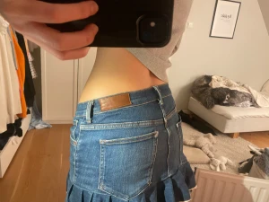 Blå jeanskjol med volangkant - Säljer en blå jeanskjol med volangkant och råa kanter längst ner. Kjolen har klassiska jeansfickor både fram och bak, bälteshällor och knappstängning. Perfekt för dig som gillar en trendig och avslappnad stil.