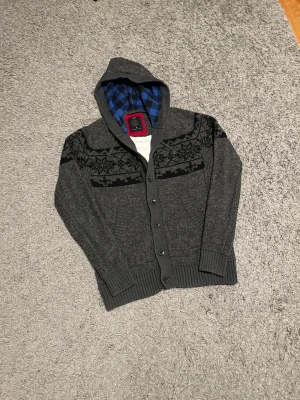Stickad cardigan med luva - Säljer en trendig stickad cardigan med knappar och luva! Tröjan är i nyskick 9/10. Inga defekter!! Tröjan har en klassiskt rutigt mönster i luvan. 🤩  Tveka inte på att höra av dig!💪🏼