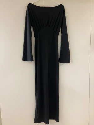 Svart långklänning med slits från nakd - Svart långklänning från nakd med vida långa ärmar, rundad halsringning och har en slits baktill. Endast använd ett fåtal gånger