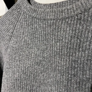Grå stickad tröja med rund hals - Mysig grå stickad tröja med rund halsringning och ribbad struktur. Långärmad modell som är perfekt för kyligare dagar. Enkel och stilren design som passar till det mesta. 