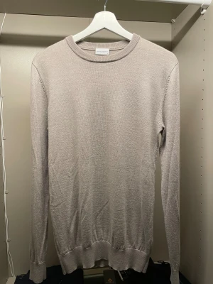 Beige stickad merinoull tröja John Henric - Snygg beige stickad merinoull tröja från John Henric i storlek S. Tröjan har rund hals, ribbade muddar och lång ärm. Perfekt för dig som gillar stilrena och enkla plagg med en soft vibe. Materialet är mjukt och skönt, passar till många olika looks.