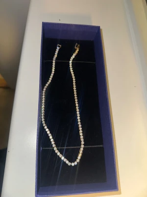 Matrix tennishalsband  - Ett snyggt halsband med glittrande strass-stenar i rad på en silverfärgad kedja. Perfekt för dig som vill sticka ut med lite extra bling. Kedjan är tunn och smidig, och stenarna ger ett riktigt lyxigt intryck. Låset är i metall och halsbandet levereras i en blå ask. Nypris 3000kr