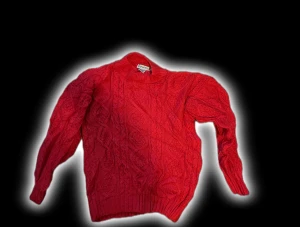 Röd stickad polotröja från Carraig Donn - Riktigt snygg röd polotröja från Carraig Donn med grovstickat kabelmönster och ribbade muddar. Tröjan har lång ärm och hög krage som ger extra cozy vibe. Perfekt för dig som gillar färg och vill sticka ut lite extra.