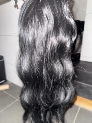 Svart lång syntetisk peruk med tillbehör - Säljer en svart lång peruk med vågigt hår från Dola Hair. Peruken har justerbara band på insidan för perfekt passform och är gjord av syntetmaterial. Medföljer hårvårdsprodukter, hårnät och ett svart/pink Dola Hair pannband. Perfekt för att byta stil snabbt!värmetålig.