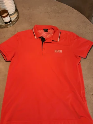 Röd Hugo Boss pikétröja M - Snygg röd pikétröja från Hugo Boss i klassisk design med vit logotyp på bröstet. 