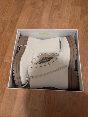 Beige boots från Catwalk strl 38 - Snygga beige boots från Catwalk med grov brunsula, snörning och dragkedja på sidan. Tillverkade i syntetmaterial med rund tå och platt sula. Perfekta för dig som vill ha en clean och trendig look till höst och vinter. Nypris 599💕