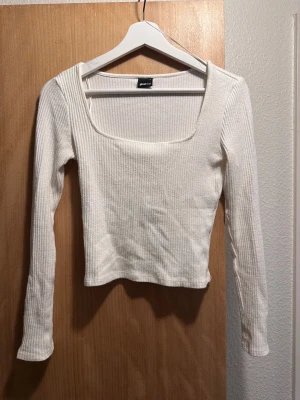 Vit ribbad topp från Gina Tricot - Säljer en vit långärmad topp från Gina Tricot i storlek S. Toppen har en fyrkantig urringning och är croppad i modellen. Materialet är ribbad och stretchigt, vilket gör den både bekväm och snygg. 