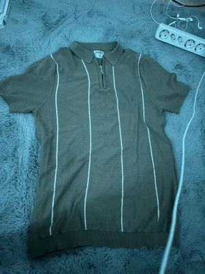 Beige pikétröja med dragkedja från SAMS -  M men passar oxå S. Tröjan har korta ärmar, krage och en halv dragkedja framtill. Den är stickad i bomull och har vita vertikala ränder som ger en clean och retro vibe. Perfekt för dig som gillar klassisk stil med en twist.