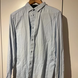 Ljusblå skjorta med knappar - Snygg ljusblå skjorta med klassisk krage och långa ärmar. Skjortan har en stilren design med knappar framtill och är tillverkad i mjukt bomullstyg. Perfekt för dig som gillar enkel och clean stil.
