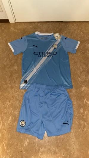 Manchester City fotbollströja Puma - Manchester City matchtröja från Puma i ljusblått med vita detaljer och klubbmärke på bröstet. Kortärmad med rund hals och tryck 'Khusanov 45' på ryggen. Materialet är lätt och ventilerande polyester, perfekt för träning eller match.