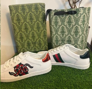 Gucci Ace sneakers med orm söker byte - Säljer ett par vita Gucci Ace sneakers i skinn med klassiska gröna och röda ränder på sidan och broderad orm. Baksidan har metallicröd och metallicgrön detalj med Gucci-logga. Platt sula, rund tå och snörning. Kommer med originalkartong och certifikat.