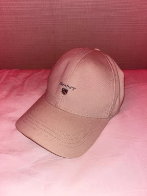 Beige keps från GANT one size helt ny oanvänd! - Snygg beige keps från GANT med klassisk böjd skärm och broderad logga framtill. Tillverkad i mjuk bomull och har stilrena sömmar som ger en clean look. Passar dig som gillar enkel och tidlös stil. Justerbar baktill för perfekt passform.