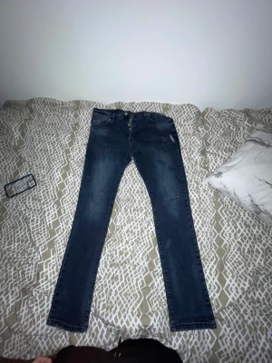 Dsquared2 Mörkblå  jeans med slitningar - Säljer ett par mörkblå skinny jeans med snygga slitningar och klassisk femficksdesign. Jeansen har knappgylf och smal passform som sitter tajt längs benen. Perfekt för dig som gillar en modern och stilren look.