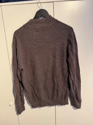 Halfzip - Snygg brun stickad tröja från Lexington med halv dragkedja och ribbad struktur. Tröjan har långärmade och en liten Lexington-logga på bröstet. Perfekt för dig som gillar klassisk stil med en modern touch.