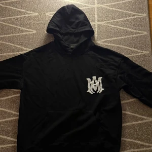 Svart  Amiri hoodie - Säljer en Svart hoodie från Amiri i helt nyskick med stor vit logga på ryggen och mindre tryck framtill. Storlek S. Pris kan diskuteras 