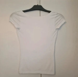 Open back topp - Säljer en vit, tight topp från Gina Tricot i storlek XS. Toppen har korta ärmar med lätt rynk vid axlarna och en djup rundad rygg. Materialet är mjukt och stretchigt, perfekt för dig som gillar en slim passform och enkel stil.