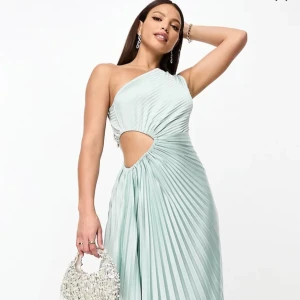 Ljusblå plisserad oneshoulder-klänning - Superfin ljusblå långklänning med plisserat tyg och oneshoulder-design. Klänningen har en snygg cut-out vid midjan och ett elegant fall. Perfekt för dig som vill sticka ut med en modern och trendig look. Storlek 38  använda en gång 