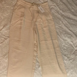 Beiga linne byxor från Calvin Klein  - Snygga oanvända beiga byxor från Calvin Klein Jeans med raka ben och dragsko i midjan. Byxorna har fickor fram och bak samt diskret logga bak. Tillverkade i mjuk bomull för en clean och chill look. Tyvärr stor på mig