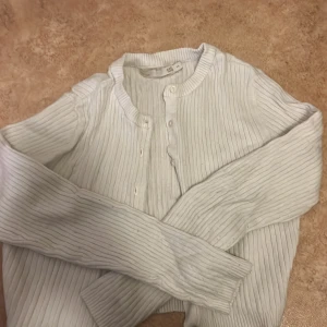 Vit ribbad kofta från 157 - Säljer en vit ribbad kofta från 157 i storlek XS. Koftan har långa ärmar, rund halsringning och knäppning framtill med matchande knappar. Perfekt att slänga över en topp för en chill och stilren look.