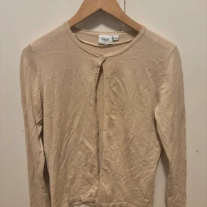 Beige kofta från Saint Tropez - Snygg beige kofta från Saint Tropez i storlek M. Koftan har rund halsringning, långa ärmar och knäppning framtill med små matchande knappar. Perfekt att slänga över en topp för en enkel och clean look. Frakt ingår ej💕