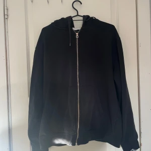 Svart hoodie med dragkedja och huva - Svart hoodie med dragkedja framtill och huva med snörning. Tröjan har känguruficka och långa ärmar, perfekt för chill dagar. Tillverkad i mjukt bomullsmaterial för extra komfort. Sparsamt använd💕