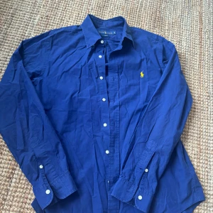 Blå skjorta från Ralph Lauren - Klassisk blå skjorta från Ralph Lauren i slim fit-modell. Skjortan har långa ärmar, knappar framtill och den ikoniska gula loggan broderad på bröstet. Tillverkad i mjuk bomull och passar perfekt till jeans eller chinos. Skriv ifall de finns frågor eller du vilse fler bilder, kolla gärna min profil ❣️❣️❣️