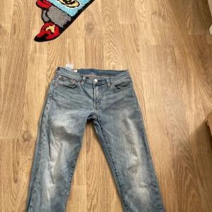 Levi's 511 ljusblå jeans W28 L32 - Säljer ett par Levi's 511 jeans i ljusblå tvätt med klassisk femficksdesign och smal passform. Jeansen har subtila slitningar framtill och bak, samt ikonisk läderpatch bak i midjan. Perfekta för dig som gillar en clean och tidlös look.