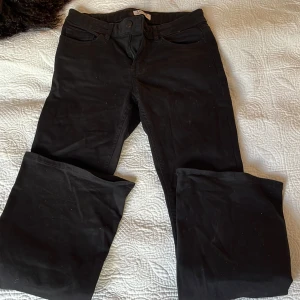 Svarta bootcut/flared jeans Lindex  - Säljer ett par svarta jeans med bootcut-modell. Byxorna har klassisk femficksdesign, hällor för bälte och stängs med knapp och dragkedja. Materialet är jeans och färgen är helsvart, vilket gör dem enkla att matcha med olika stilar.