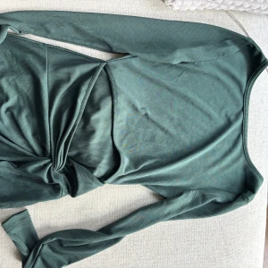 Grön ribbad klänning - Säljer en snygg grön ribbad klänning med långa ärmar och öppet vid midjan. Klänningen har en tight passform och är tillverkad i ett mjukt, stretchigt material som sitter skönt på kroppen. Perfekt för dig som gillar stilrena och trendiga plagg. Skulle säga den passar Xs/S