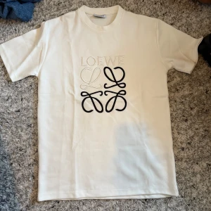 Vit Loewe t-shirt  - Loewe Tröja – Vit (Ny) 👕 Storlek: M 🤍 Färg: Vit ✨ Skick: 10/10 – helt ny, aldrig använd 🏷️ Detaljer: Etikett kvar (ange om den finns kvar) 💎 Märke: Loewe