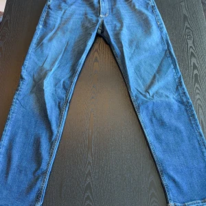 Blå jeans Jack & Jones Clark 32/32 - Snygga blå jeans från Jack & Jones, modell Clark Regular. Klassisk femficksdesign med raka ben och normal passform. Jeansen har tydliga kontrastsömmar och är tillverkade i slitstarkt denim. Perfekta för en avslappnad och stilren look.