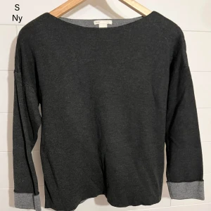 Mörkgrå långärmad tröja storlek S - En stilren mörkgrå långärmad tröja från HM i mjukt material. Tröjan har en enkel, rak passform och bredare muddar i ljusare grått vid ärmsluten. Perfekt för en chill och avslappnad look.