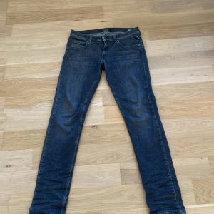 Svarta jeansbyxor från Replay - Säljer ett par svarta jeansbyxor från Replay med klassisk femficksdesign och raka ben. Jeansen har normal passform och är tillverkade i ett mjukt denimtyg. Perfekta för dig som gillar stilrena och tidlösa jeans. På båda bakfickorna är de ett litet märke men syns inget. 
