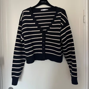 Randig kofta från Zara - Snygg svart och vit randig kofta från Zara med v-ringning och knappar framtill. Croppad modell med långa ärmar och ribbade muddar. Strl L och knappt använd!