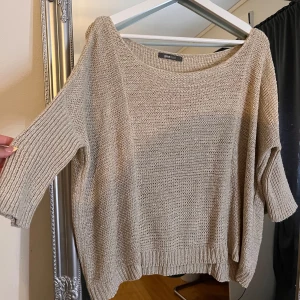 Beige stickad tröja från Gina Tricot - Beige stickad tröja från Gina Tricot med avslappnad passform och bred halsringning. Tröjan har trekvartsärmar och ribbade muddar vid ärmslut och nederkant. Perfekt för lager-på-lager och chill vibes.