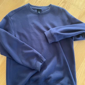 Mörkblå sweatshirt från H&M, stl S - En basic mörkblå sweatshirt från H&M i storlek S. Tröjan har rund halsringning, ribbade muddar vid ärmslut och nederkant samt en avslappnad passform. Perfekt för en chill look och enkel att matcha med jeans eller joggers.