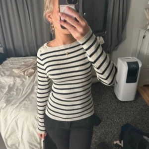 Randig ribbad tröja med knappar - Säljer en vit och svart ribbad tröja med smala ränder och snygga knappar på axlarna. Tröjan är långärmad och har en tight passform.